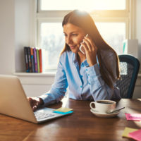 woman working on laptop in office talking on cell phone