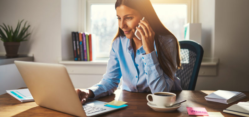 woman working on laptop in office talking on cell phone